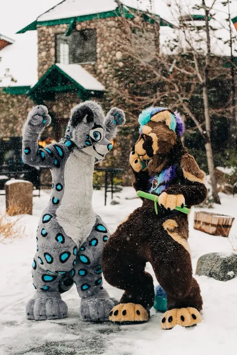 A fursuiter in a bright floral shirt posing in the snow outside a lodge